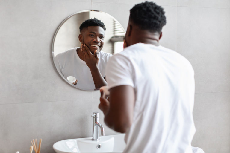 man applying moisturizer looking in the mirror
